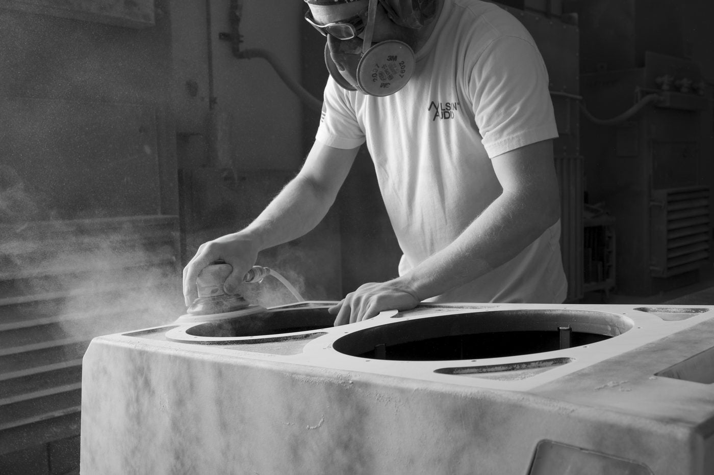 A craftsperson in a respirator sanding a woofer enclosure