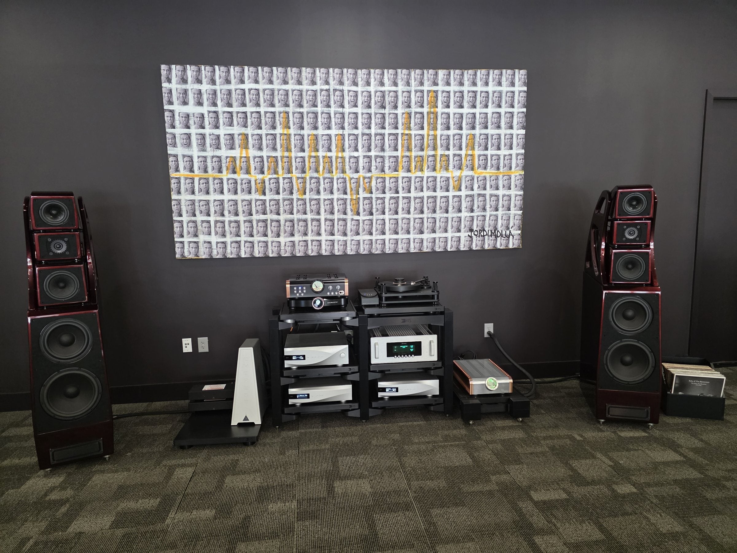 A listening setup at Sound Sanctuary Austin: a matched pair of floorstanding loudspeakers flanking a turntable and electronics rack, beneath a large grid-of-faces artwork.